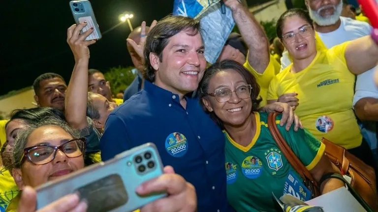 Robério Negreiros abraça uma apoiadora com a camisa da Seleção durante caminhada noturna, cercado de eleitores com adesivos do número 20.000